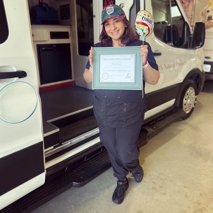 Divya holding her graduation certificate by the mobile grooming van