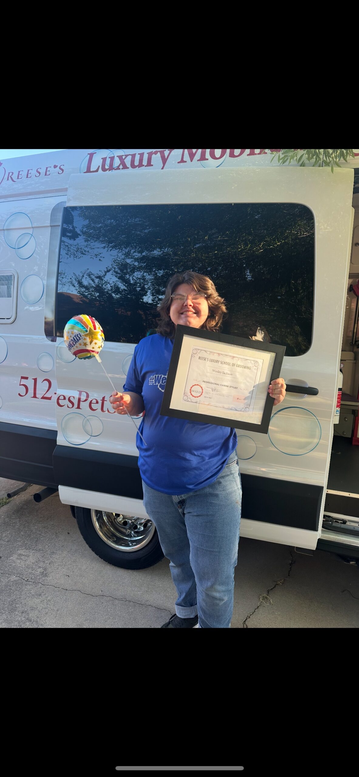 Wes holding his graduation certificate in front of the Reese's grooming van